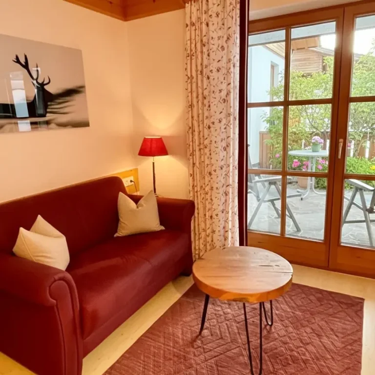 Wohnzimmer-in-der-Ferienwohung-Alpnerose-im-Haus-am-Wiesbach-mit-grosser-terasse-in-reit-im-winkl-Chiemgau Gemütliche Wohnzimmer mit Sofa, Beistelltisch und Blick auf die Terrasse in der Ferienwohnung Alpenrose im Haus am Wiesbach, reit im Winkl