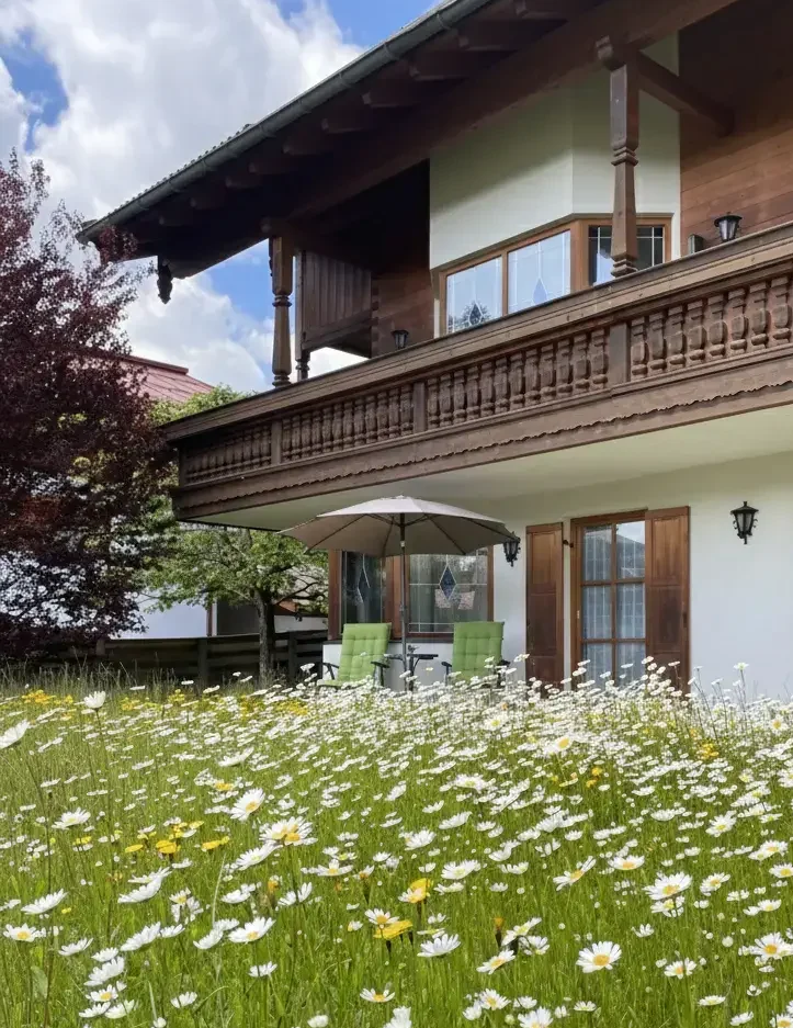 Urlaub im Haus am Wiesbach zwischen März und Juni t: Außenansicht vom Haus am Wiesbach in Reit im Winkl mit blühendem Garten und Bergblick während der Zwischensaison.