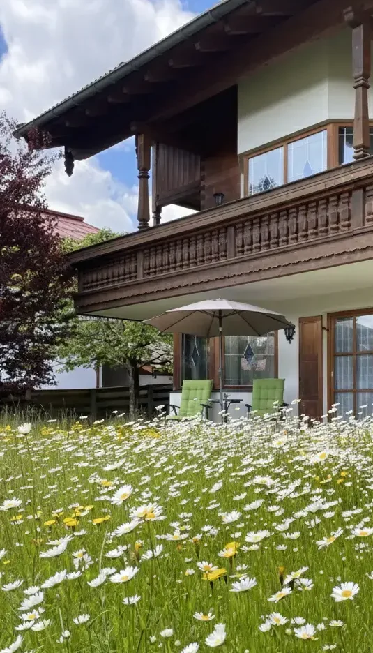 Urlaub im Haus am Wiesbach zwischen März und Juni t: Außenansicht vom Haus am Wiesbach in Reit im Winkl mit blühendem Garten und Bergblick während der Zwischensaison.